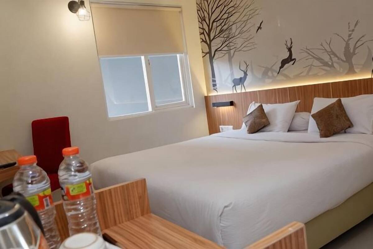 Ett hotellrum med en säng, ett träfärgat sänggavel, ett fönster och en väggmålning som föreställer rådjur och träd.