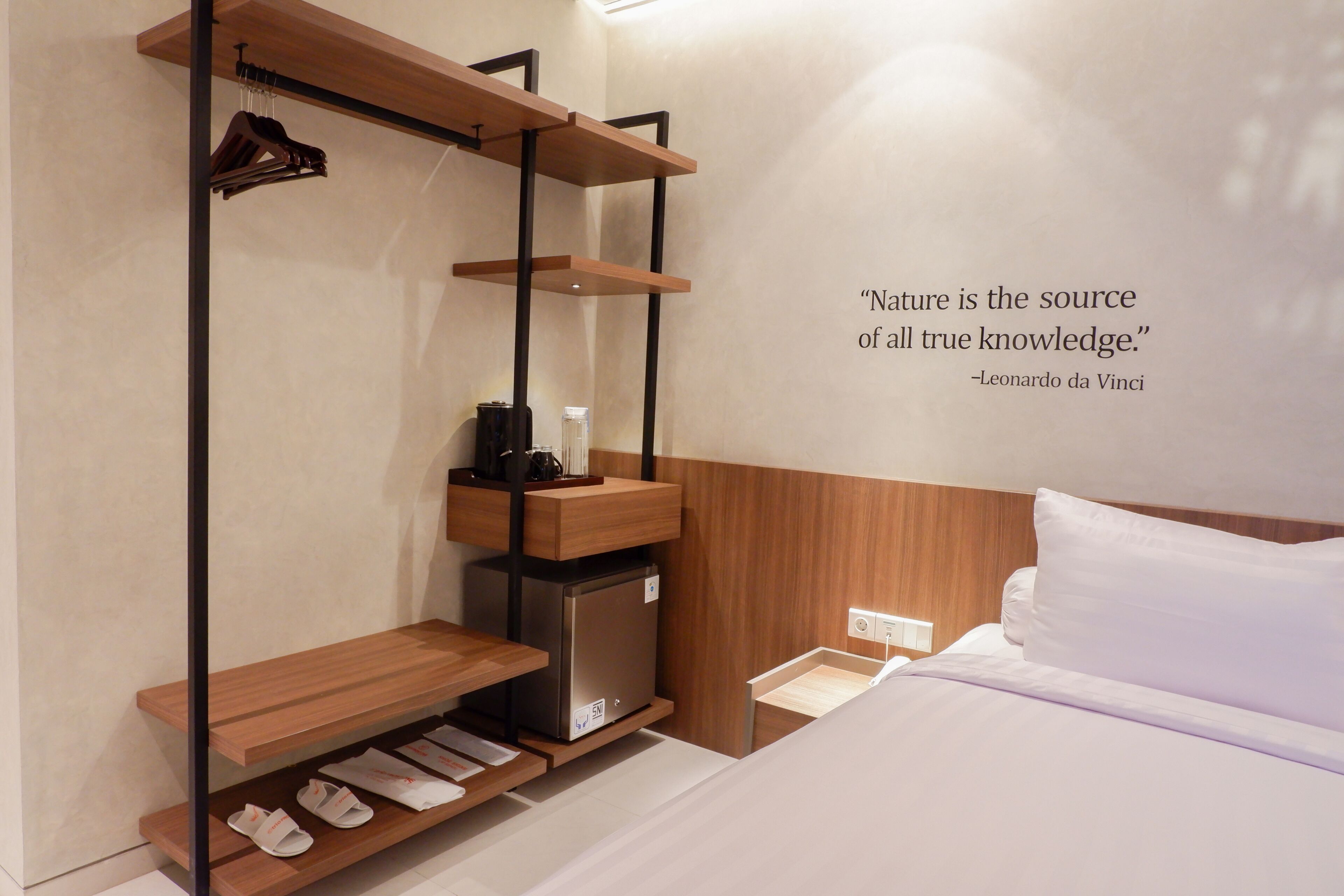 A bedroom with a bed, a shelf with shoes, a small refrigerator, and a quote on the wall.
