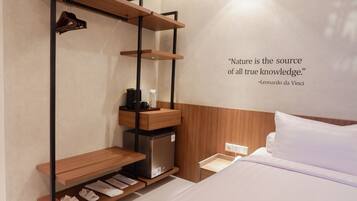 A bedroom with a bed, a shelf with shoes, a small refrigerator, and a quote on the wall.