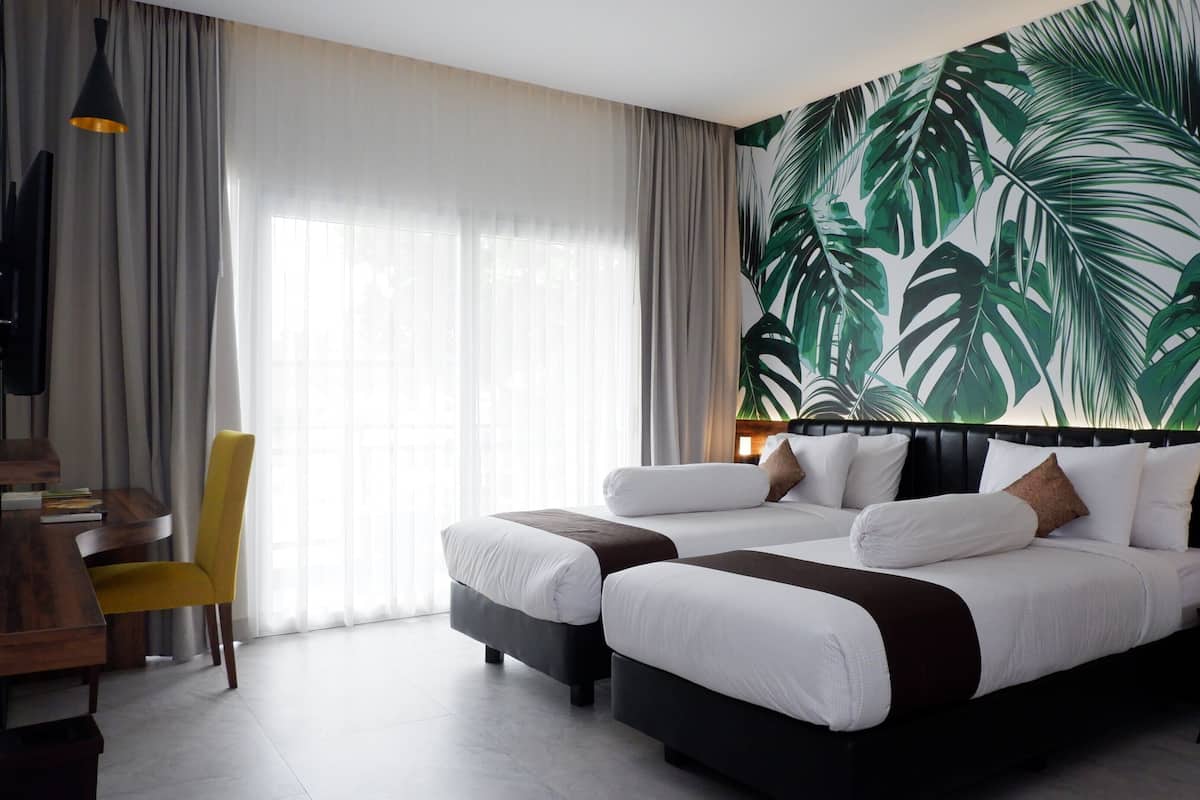 Ett hotellrum med en stor säng, ett skrivbord, en stol och en tapet med tropiska bladmotiv.