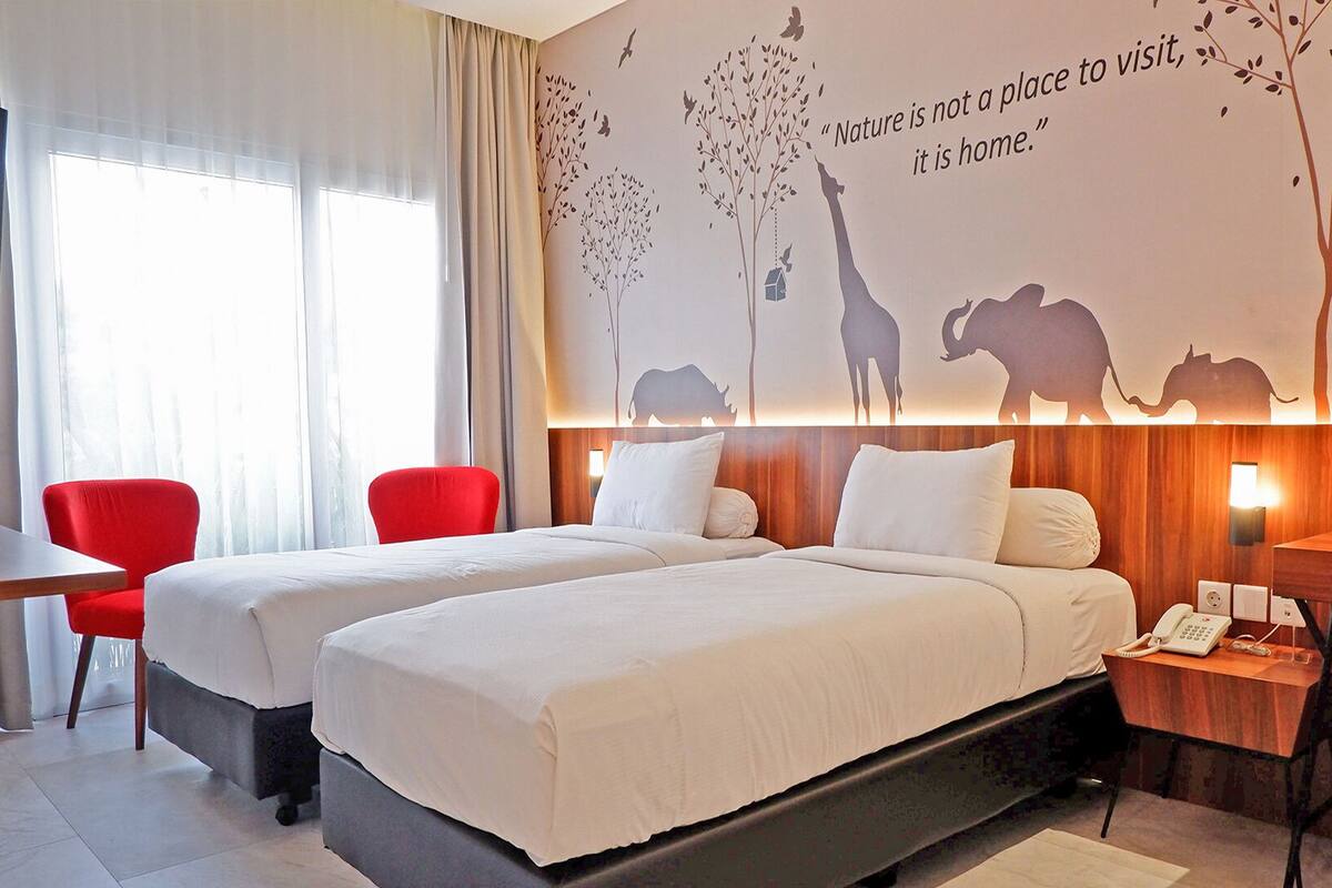 Ett hotellrum med två sängar, ett skrivbord, en stol och en väggmålning med djursiluetter och ett citat.