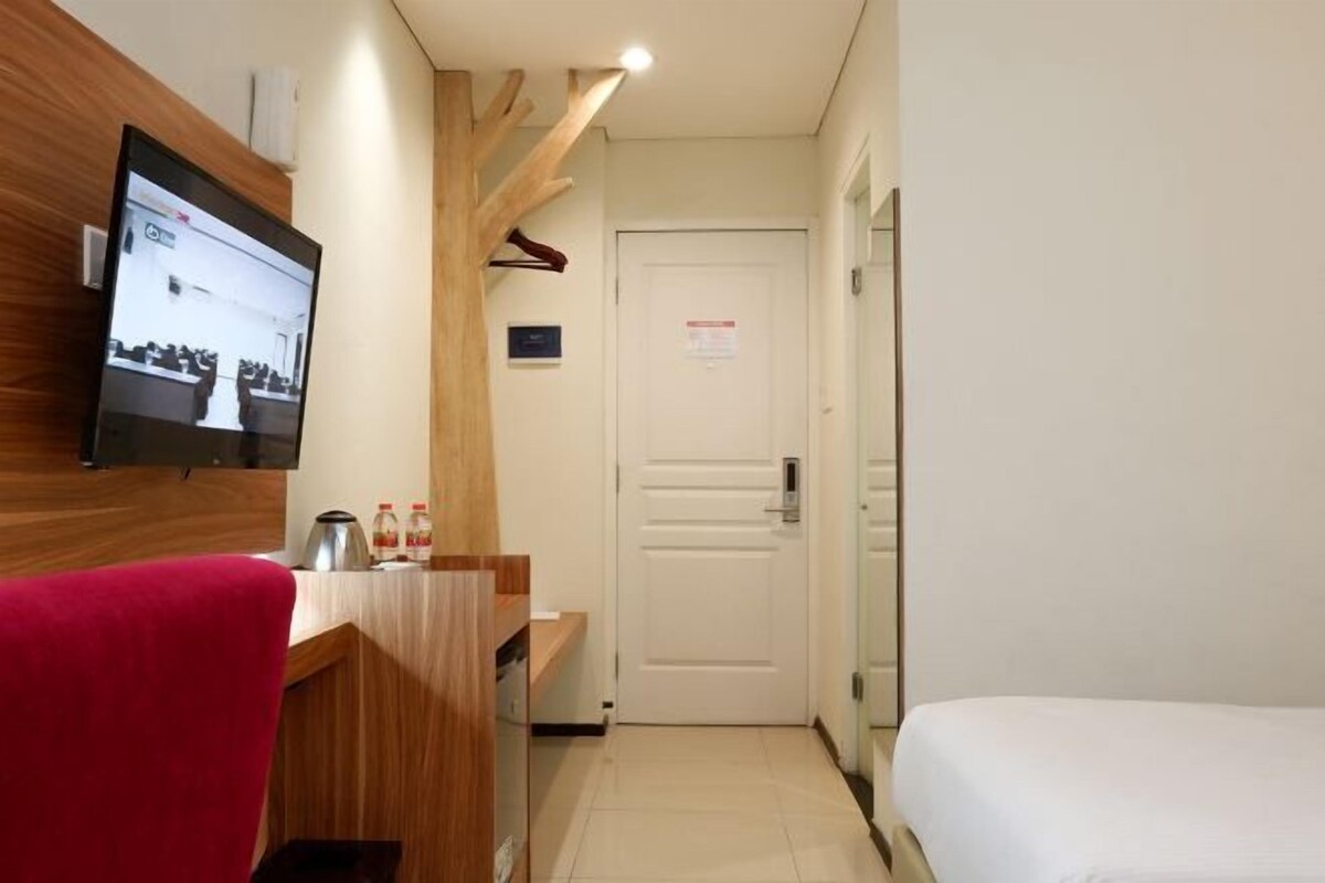 A hotel room with a wooden desk, a TV mounted on the wall, a bed, and a door with a sign.