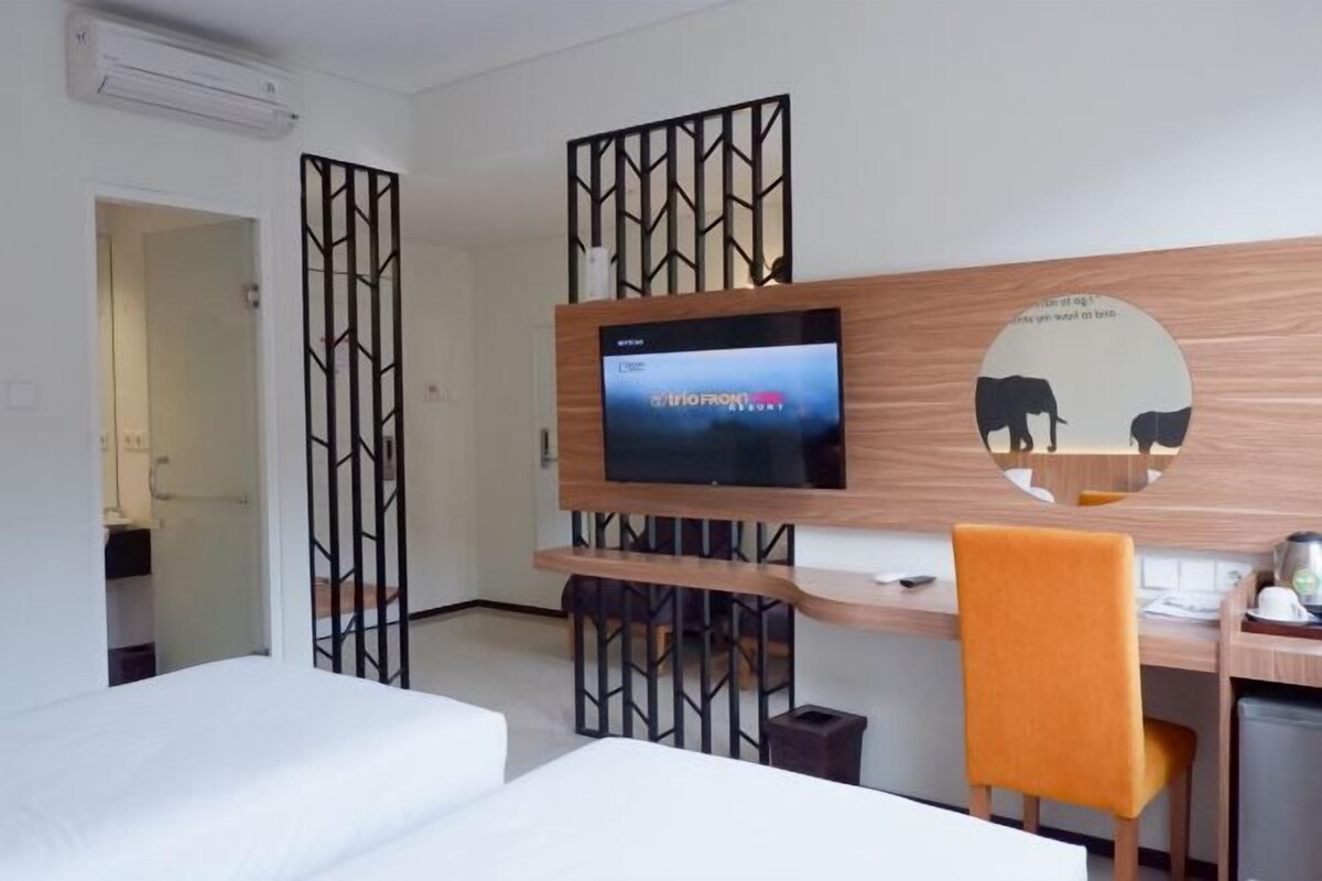 A hotel room with a TV mounted on a wooden wall, a desk with a chair, and two beds.
