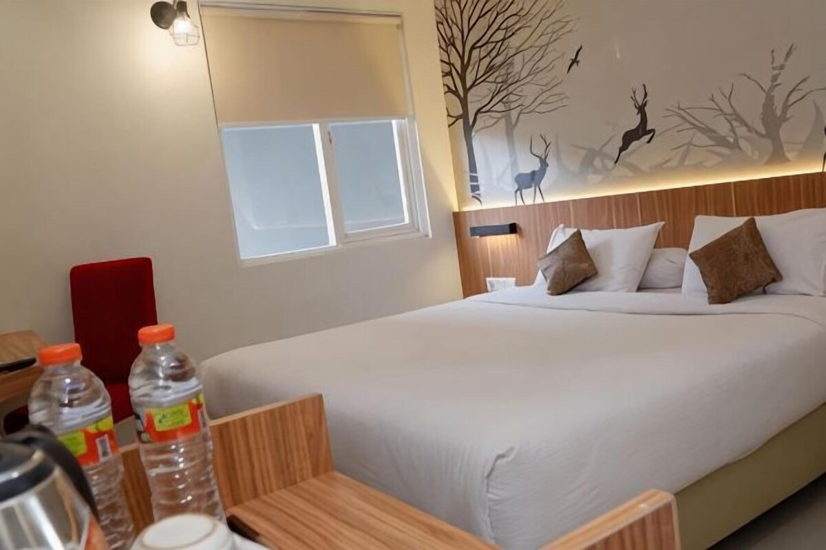 A hotel room with a bed, wooden headboard, a window, and a wall mural of deer and trees.