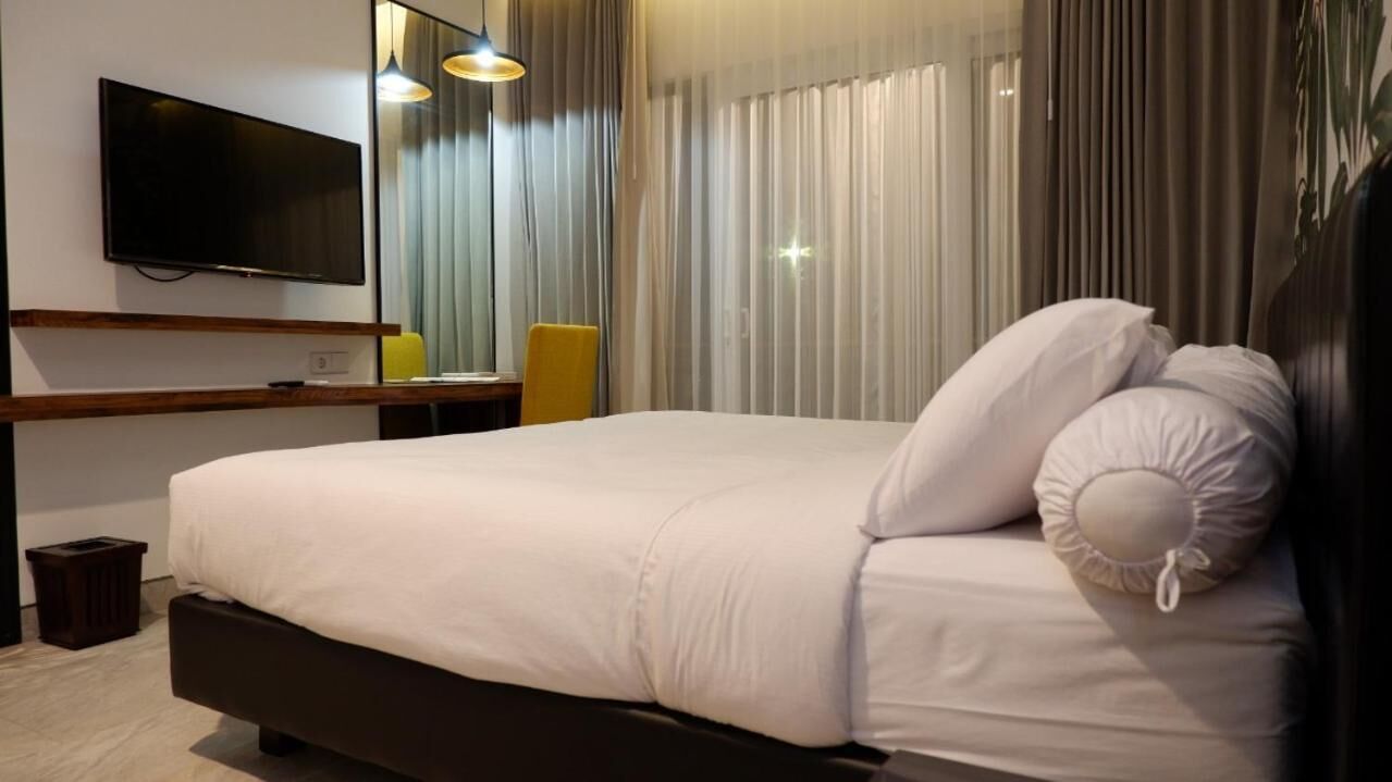 Una camera d'albergo moderna con un letto grande, una TV a schermo piatto fissata al muro e una finestra con tende leggere.