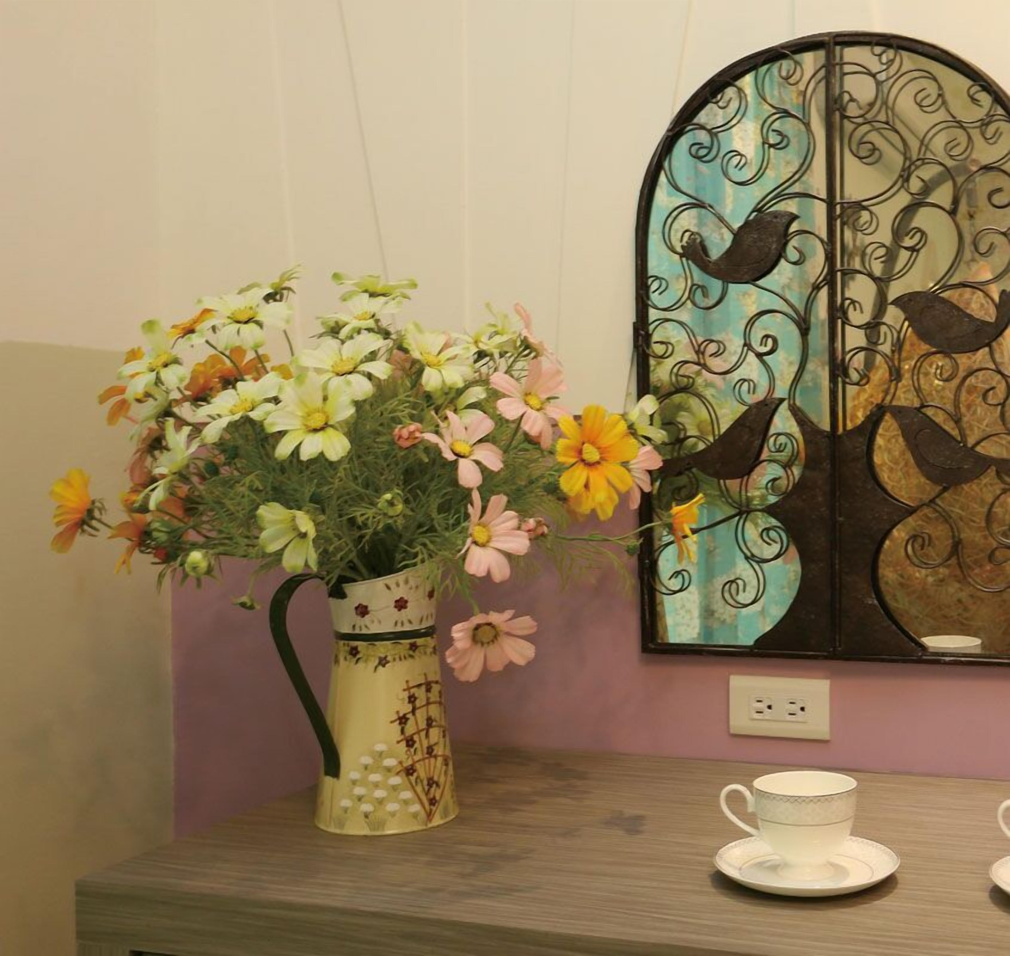 A vase with flowers on a table next to a wall-mounted mirror with a bird design.