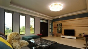 A spacious living room with a large window, a sofa, a coffee table, and a television on a wooden wall. - Jifun Flower Meanings (Ji'an)