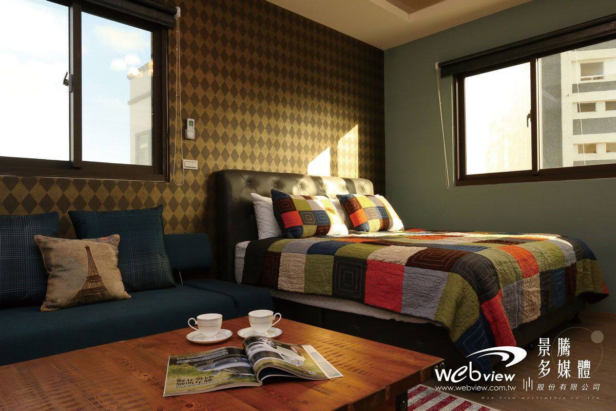 Een hotelkamer met een bed, een bank en een salontafel met een tijdschrift. Er zijn ramen aan twee zijden van de kamer.