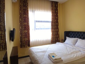 A hotel room with a bed, curtains, a window, and a wall-mounted phone. - Front One Inn Malang (Malang)