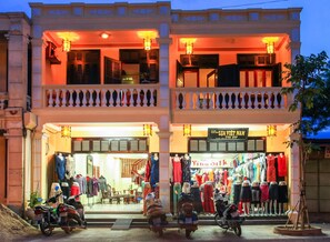 Un immeuble de deux étages doté d’un balcon et d’un magasin situé au rez-de-chaussée où sont exposés des vêtements.