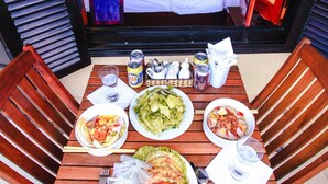 A dining table with plates of food, a bed with a white bedspread, and a bathroom visible through an open door. - Harmony Homestay (Da Nang)