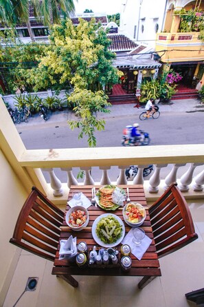 Un balcon avec une table dressée pour un repas, donnant sur une rue où sont garées des motos et où un cycliste passe.