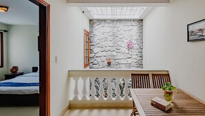 A room with a stone wall, a wooden table with chairs, a bed, and a window with a view of the sky. - Harmony Homestay (Da Nang)