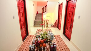 A hallway with a wooden bench, a table with food and drinks, and red doors leading to a staircase. - Harmony Homestay (Da Nang)