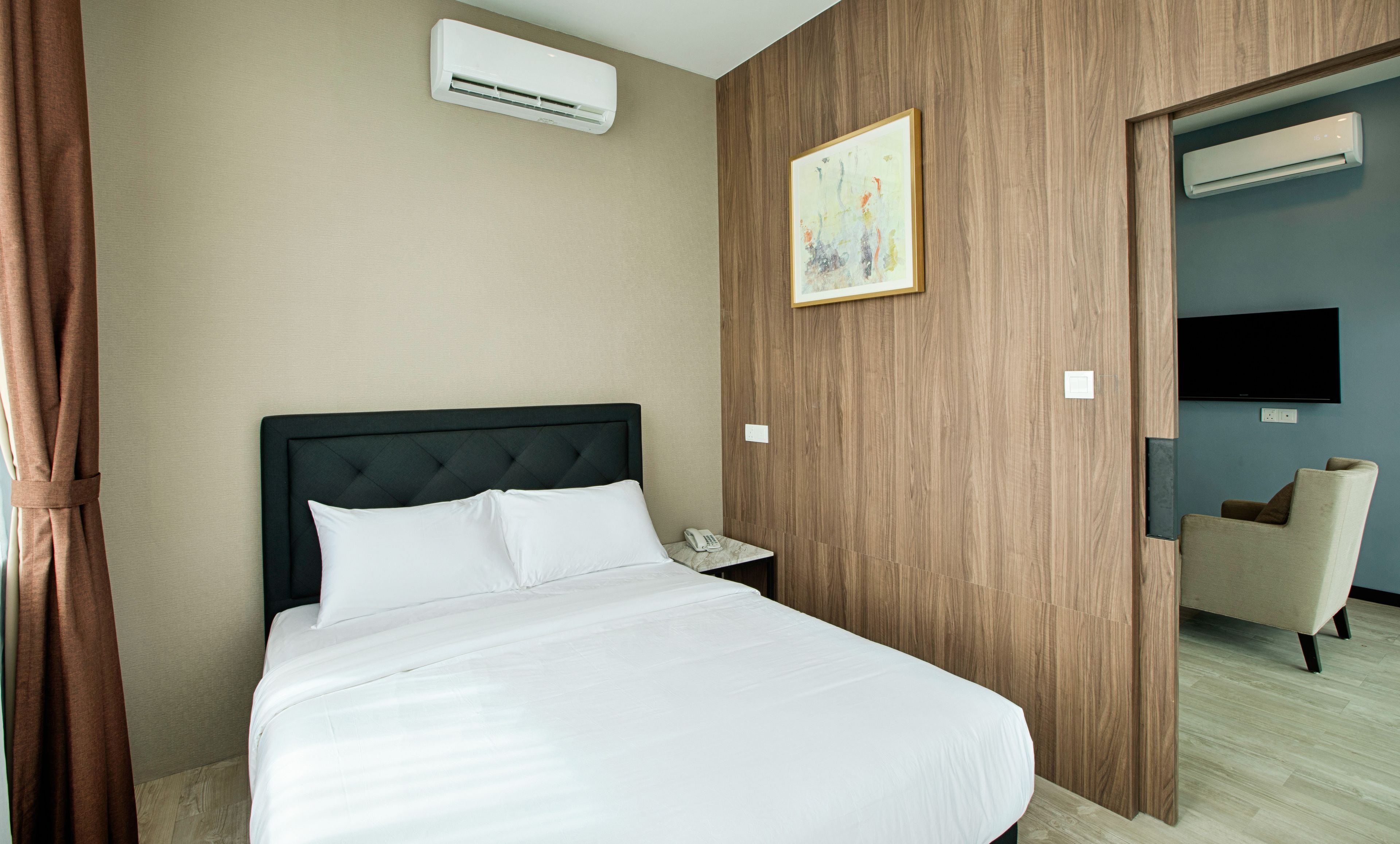 Een hotelkamer met een bed, een airconditioner, een schilderij, een televisietoestel en een stoel.