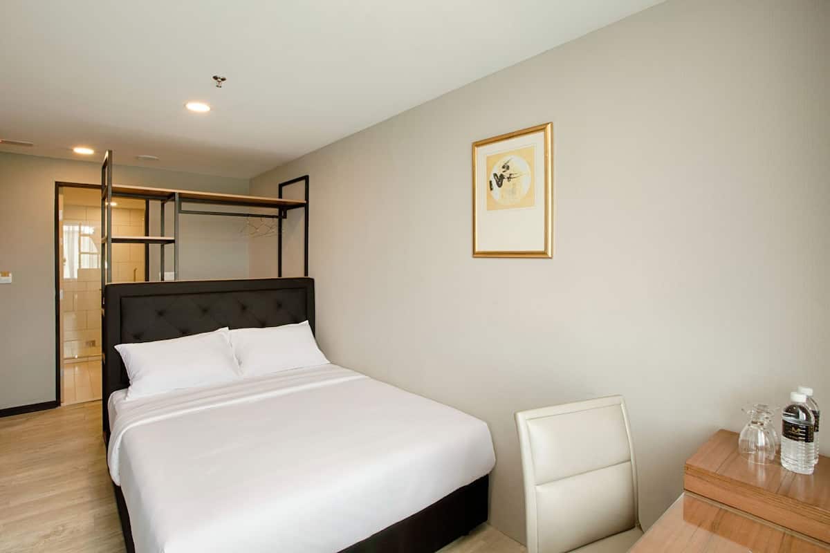 Une chambre d’hôtel avec un lit, une chaise, un bureau avec une bouteille d’eau et un tableau encadré au mur.