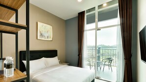 Habitación de hotel con cama, escritorio con una botella de agua, un cuadro en la pared y un balcón con sillas.