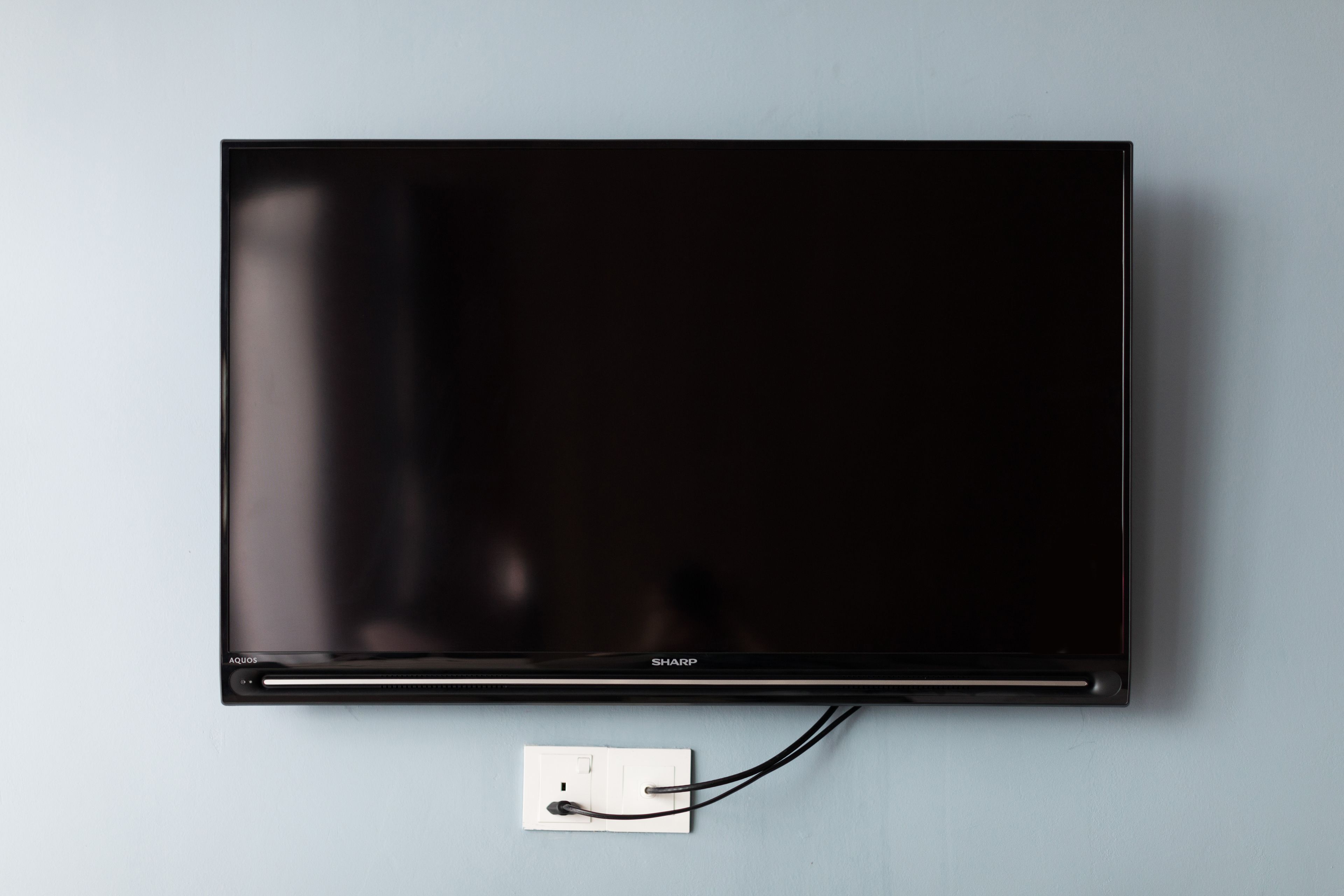 Televisor de pantalla plana montado en la pared, con el cable de alimentación conectado.