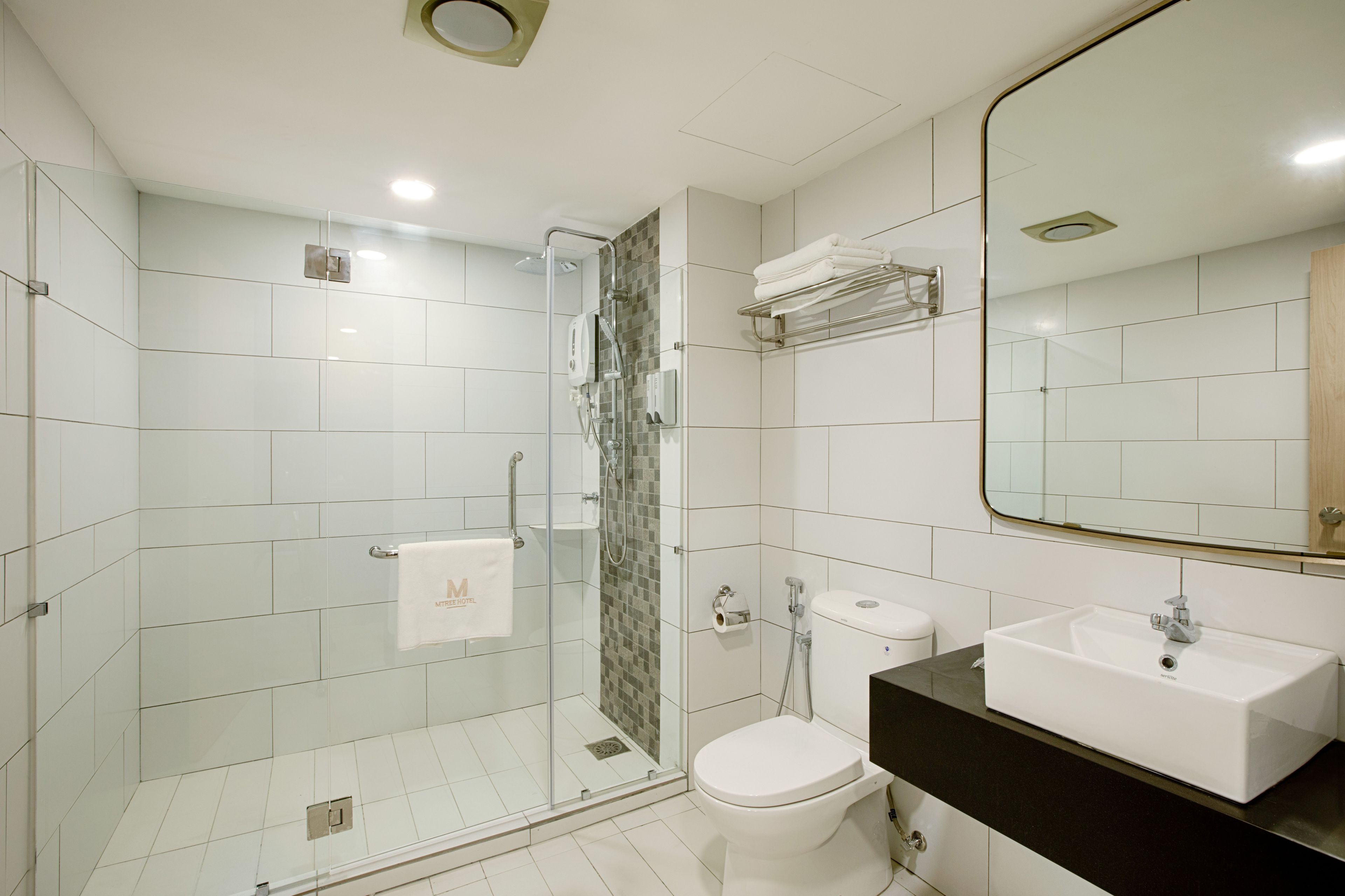 Une salle de bain moderne avec une douche à l’italienne en verre, des toilettes blanches et un plan de toilette noir avec un lavabo blanc.