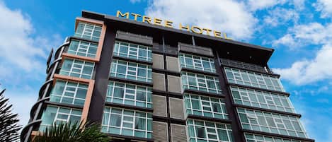 A modern hotel building with a sign reading "MTREE HOTEL" and multiple floors with large windows.