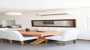 Un coin repas avec une table en bois et des chaises blanches, un luminaire suspendu moderne et un climatiseur fixé au mur.