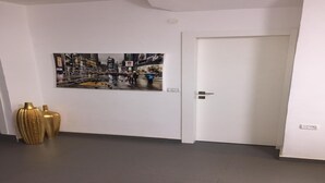 Un couloir orné d’un tableau représentant un paysage urbain, avec une porte blanche et deux vases dorés.