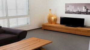Un salon comprenant un canapé, une table basse en bois, un téléviseur posé sur un meuble en bois, et deux vases dorés.