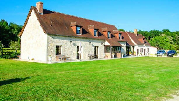 A row of stone buildings with a sloped roof, a grassy lawn, and parked cars.