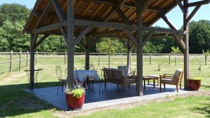 A wooden pavilion with a tiled floor, surrounded by a grassy area with a fence.