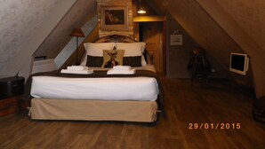 A bedroom with a large bed, a wooden headboard, a painting above the bed, and a small TV on the wall.