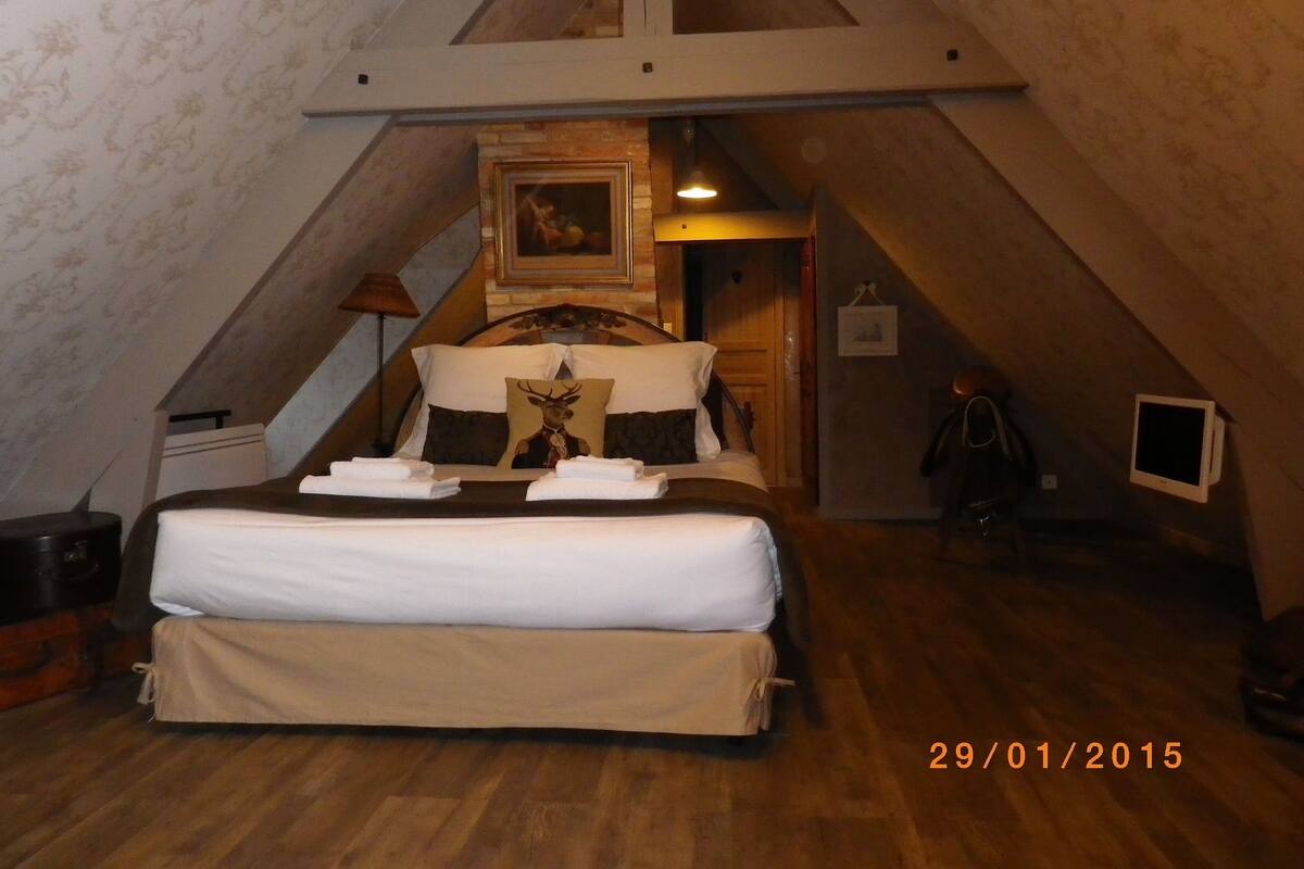 Une chambre à coucher avec un grand lit, une tête de lit en bois, un tableau au-dessus du lit et un petit téléviseur fixé au mur.