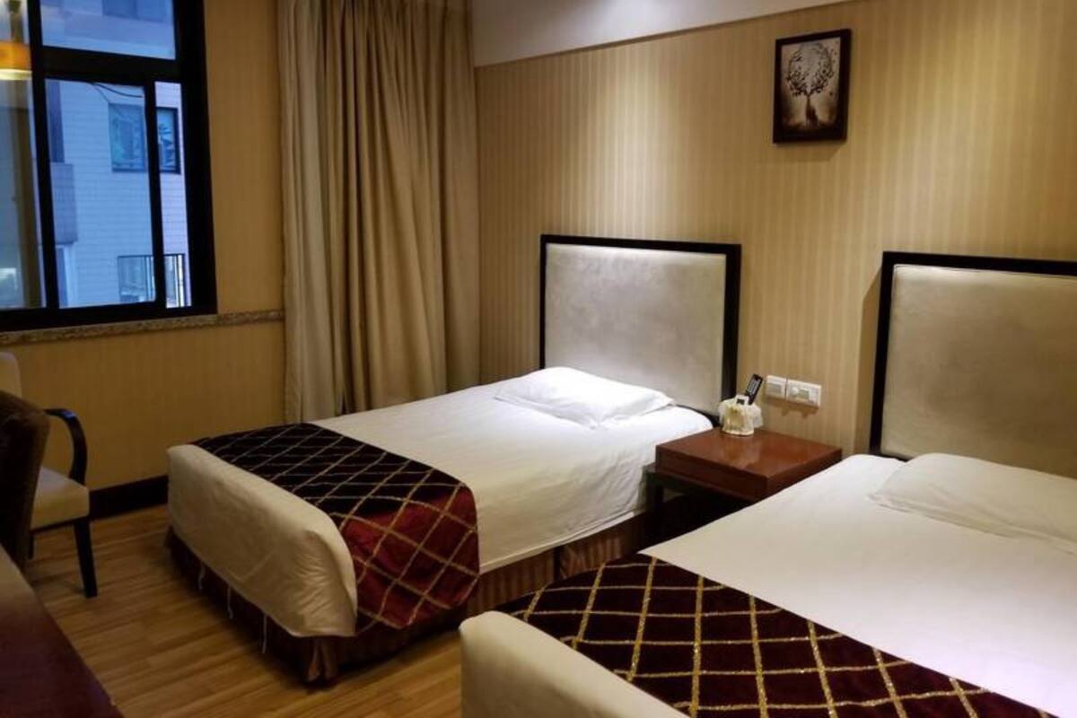 A hotel room with two beds, a window with curtains, a chair, and a wall-mounted picture.