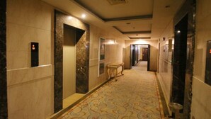 En hotellkorridor med väggar klädda i marmor, ett mönstrat golv och en hiss.