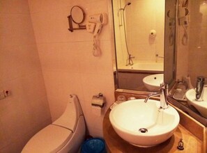 Un baño con inodoro, lavamanos, espejo y secador de pelo.
