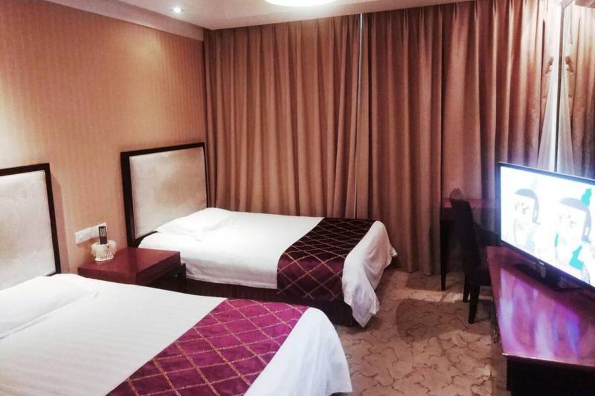 A hotel room with two beds, a television, and a large window with curtains.
