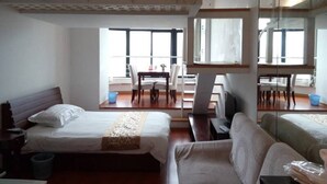 Ett hotellrum med en säng, en soffa, ett matbord med stolar och ett stort fönster.