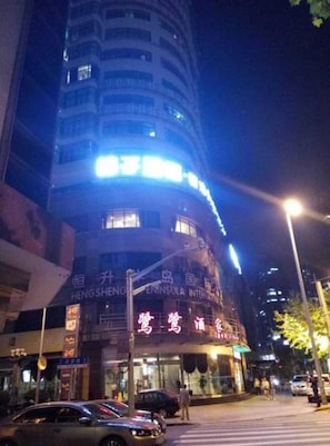 Un edificio de varios pisos con señalización iluminada y un paso de peatones en la parte delantera.