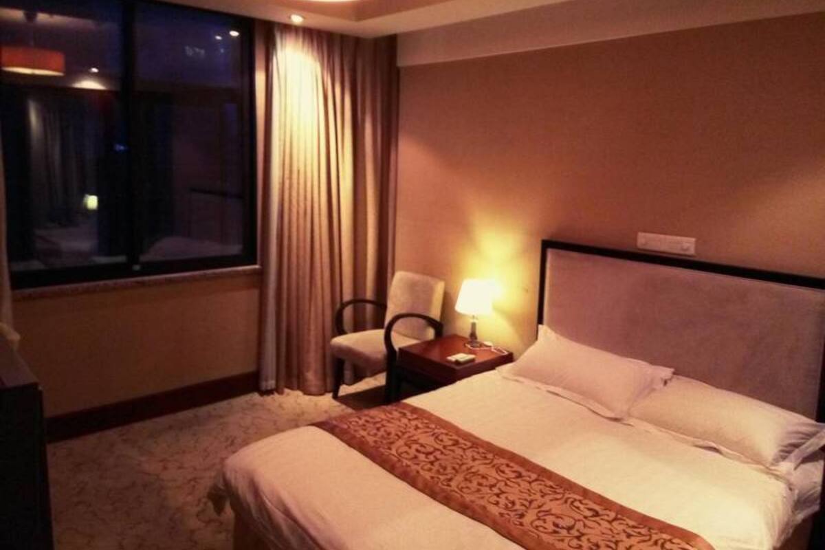 A hotel room with a large bed, a chair, a nightstand with a lamp, and a window with curtains.