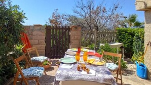 An outdoor dining area with a table set for two, surrounded by chairs, a wooden fence, and various plants. - Nice apartment in Porto Alabe with WiFi (Porto Alabe)