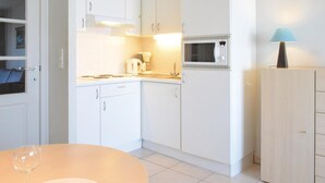 Une cuisine compacte avec des meubles blancs, un four à micro-ondes et une table avec un verre.