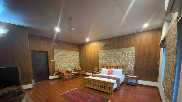 A spacious bedroom with a large bed, a wooden headboard, a nightstand, a bedside table, and a patterned wall.