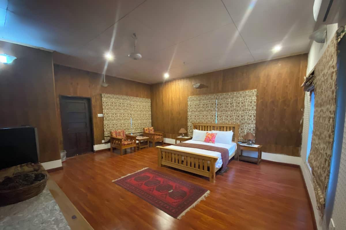 Un dormitorio amplio con una cama grande, un cabecero de madera, una mesita de noche y un papel tapiz estampado.