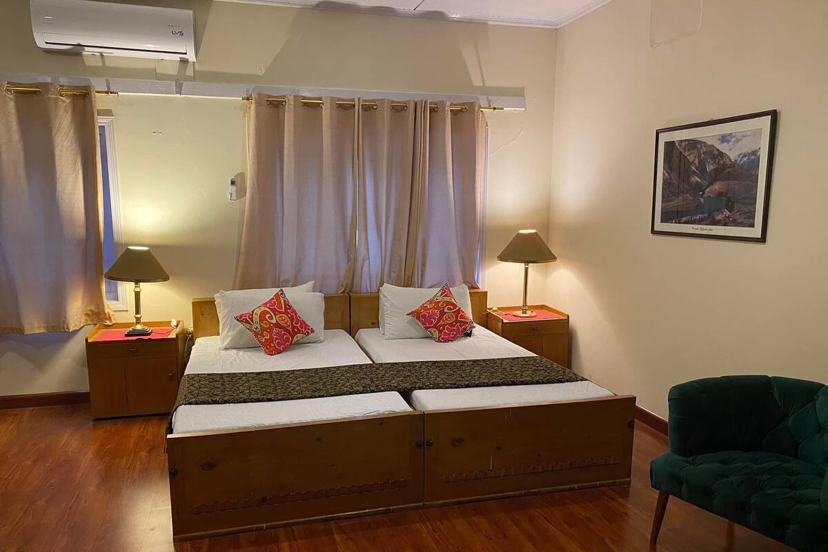 Una habitación de hotel con una cama grande, dos mesitas de noche con lámparas, un sillón verde y un cuadro en la pared.