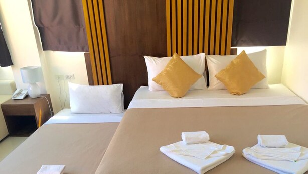 Habitación de hotel con dos camas, cada una con ropa de cama blanca y beige, y cabeceros de madera. Hay toallas sobre las camas y un teléfono en la mesita de noche.