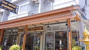 Un edificio de varios pisos con balcones, un letrero que dice 'BAAN KETKEAW GUESTHOUSE 1', y una zona de estar al aire libre con mesas y sillas.