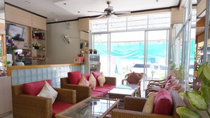 Amplia habitación con mobiliario de mimbre, una mesita de centro de vidrio y un televisor sobre una estantería.
