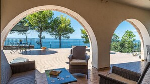 A covered outdoor seating area with wicker furniture, a table with playing cards, and a view of the sea through arches. - Nice apartment in Acciaroli with house sea view (Acciaroli)