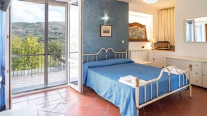 A bedroom with a bed, a nightstand, a dresser, a window with a view of greenery, and a balcony with a railing. - Nice apartment in Acciaroli with house sea view (Acciaroli)