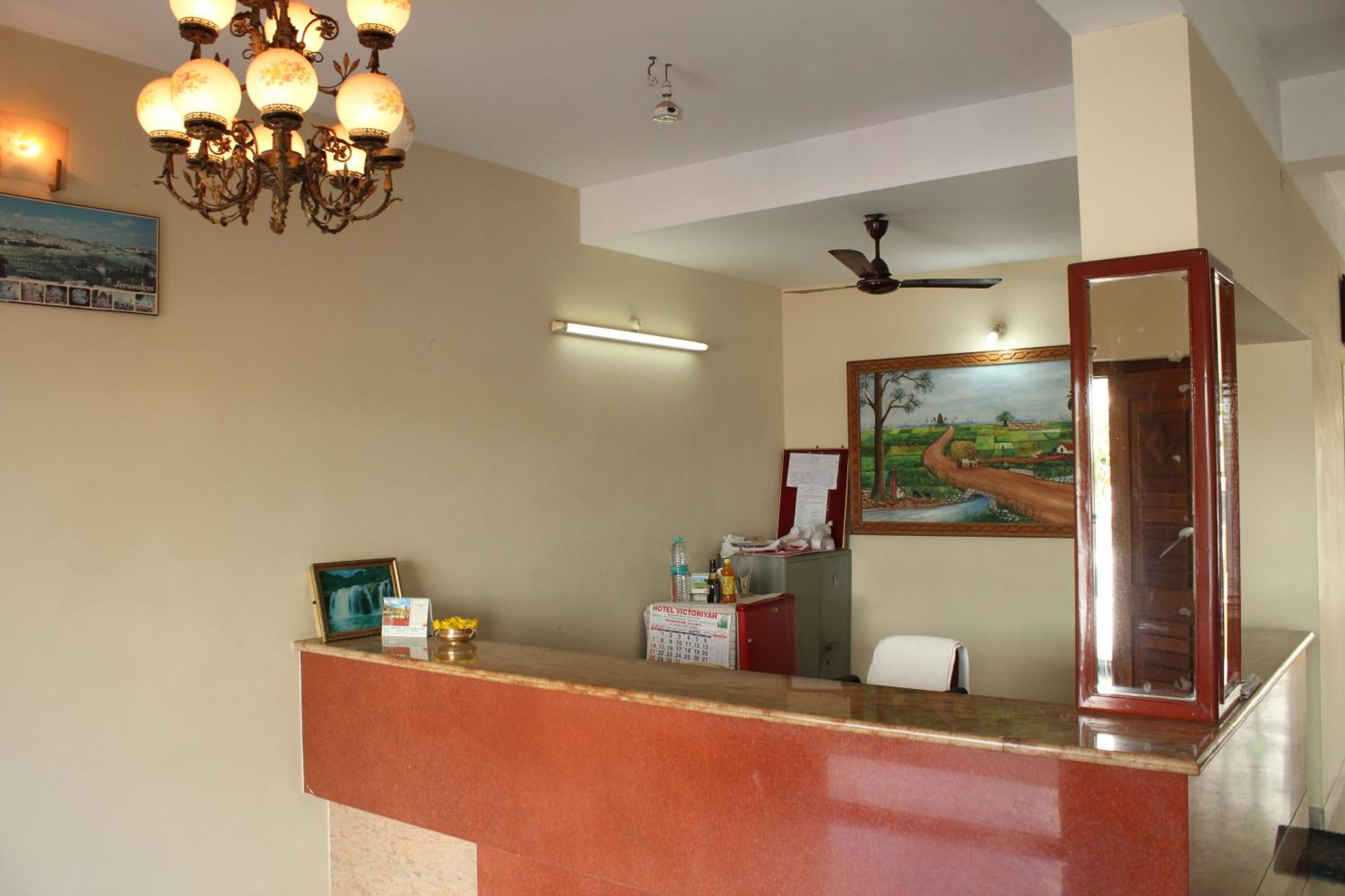 A hotel reception area with a marble counter, a chandelier, a ceiling fan, a painting on the wall, and a calendar on the counter.