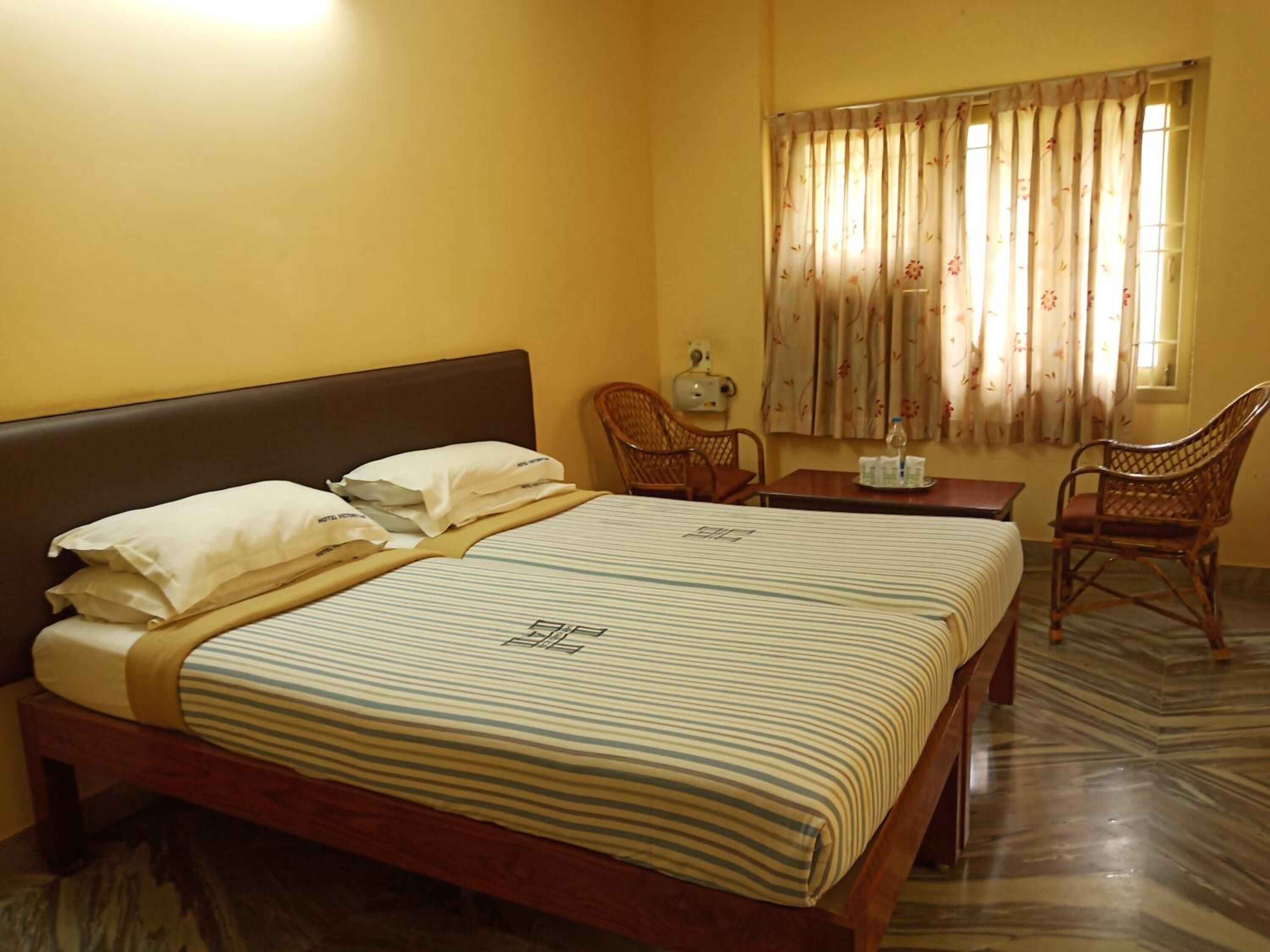 A hotel room with a bed, two chairs, a table, and a window with curtains.